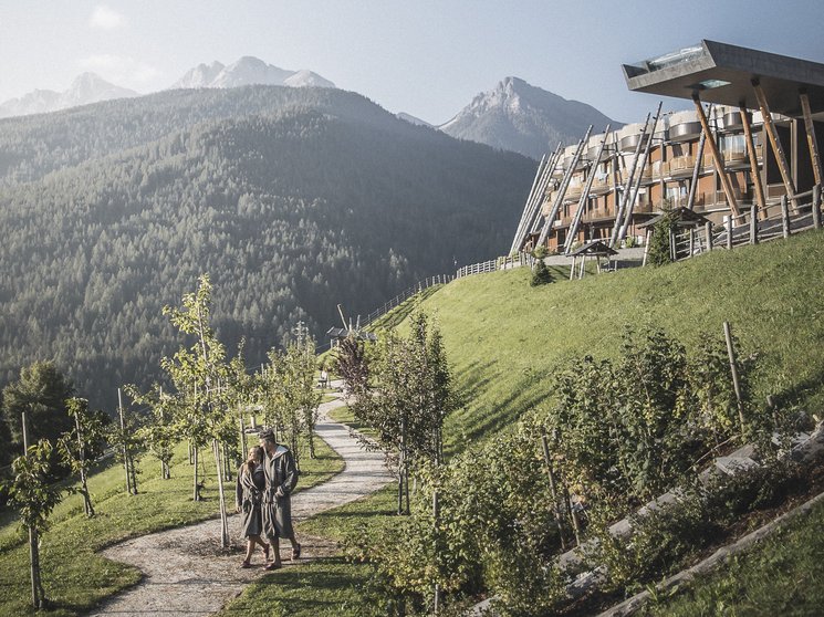 Unsere Parks, Ihre Rückzugsorte Paar spaziert auf Weg am Hang vor modernem Gebäude in bergiger Landschaft