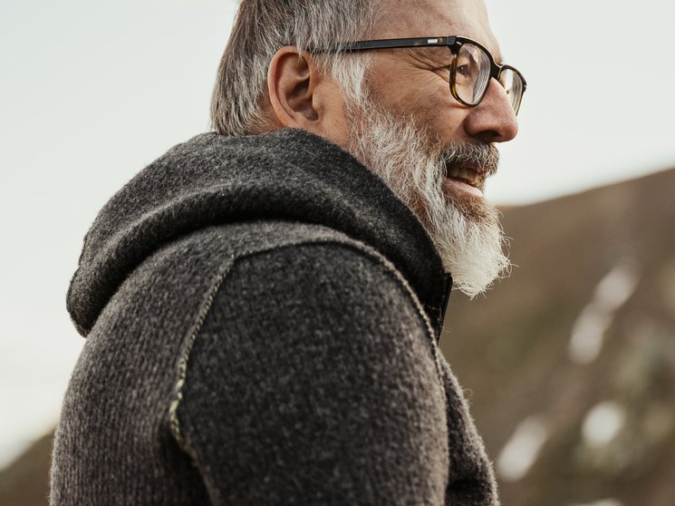 Atelier Moessmer Norbert Niederkofler Uomo anziano con occhiali e maglione grigio davanti a montagna