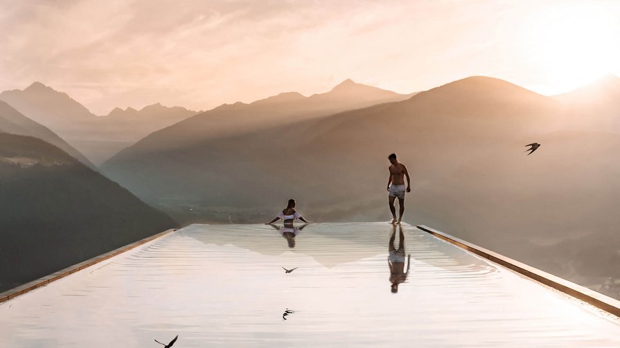 Erkunden Sie die vielfältigen Facetten des Lebens in unserem Hotel und seiner Umgebung Zwei Personen an einem Infinity-Pool mit Bergblick bei Sonnenuntergang