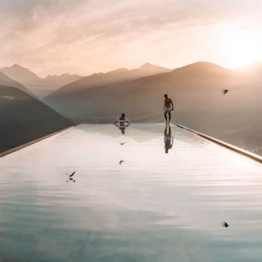 Our family-run hotel in South Tyrol Two people at an infinity pool overlooking mountains at sunset
