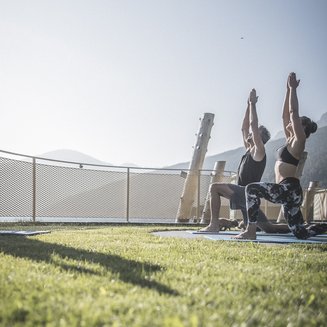 Unsere Parks, Ihre Rückzugsorte Zwei Menschen praktizieren Yoga im Freien auf einer Wiese bei Sonnenlicht