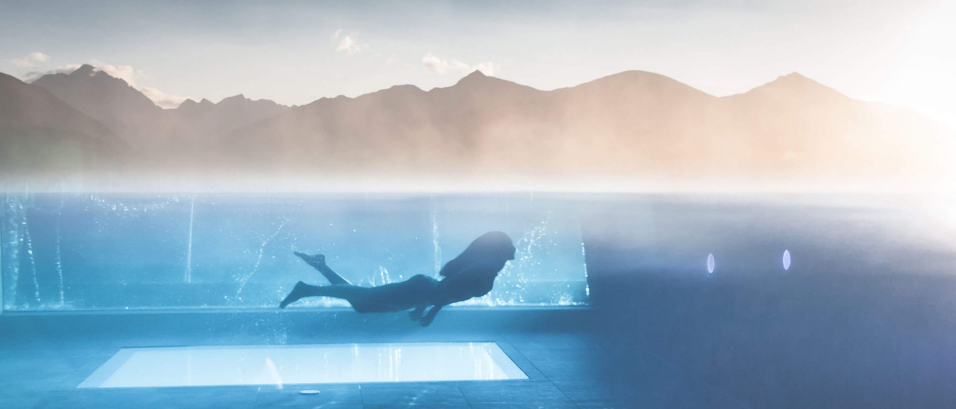 Erholung auf allen Ebenen des Seins Person schwimmt unter Wasser in einem beheizten Pool mit Bergblick
