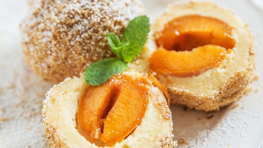 Fruchtig, locker und traditionell Marillenknödel mit Zucker und Minzblatt auf weißem Teller