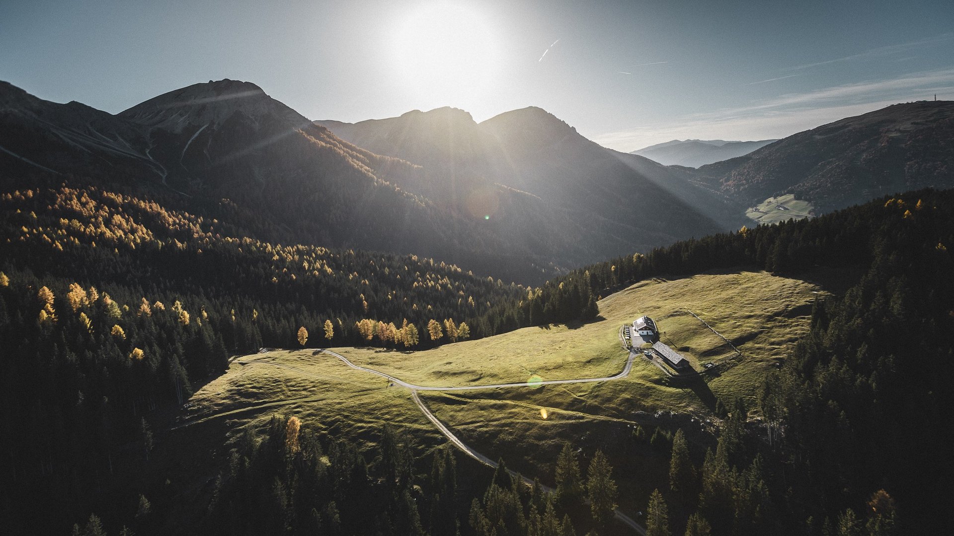 A glance at Plan de Corones/Kronplatz via webcam Sunrise over alpine meadow with houses and forest in the mountains
