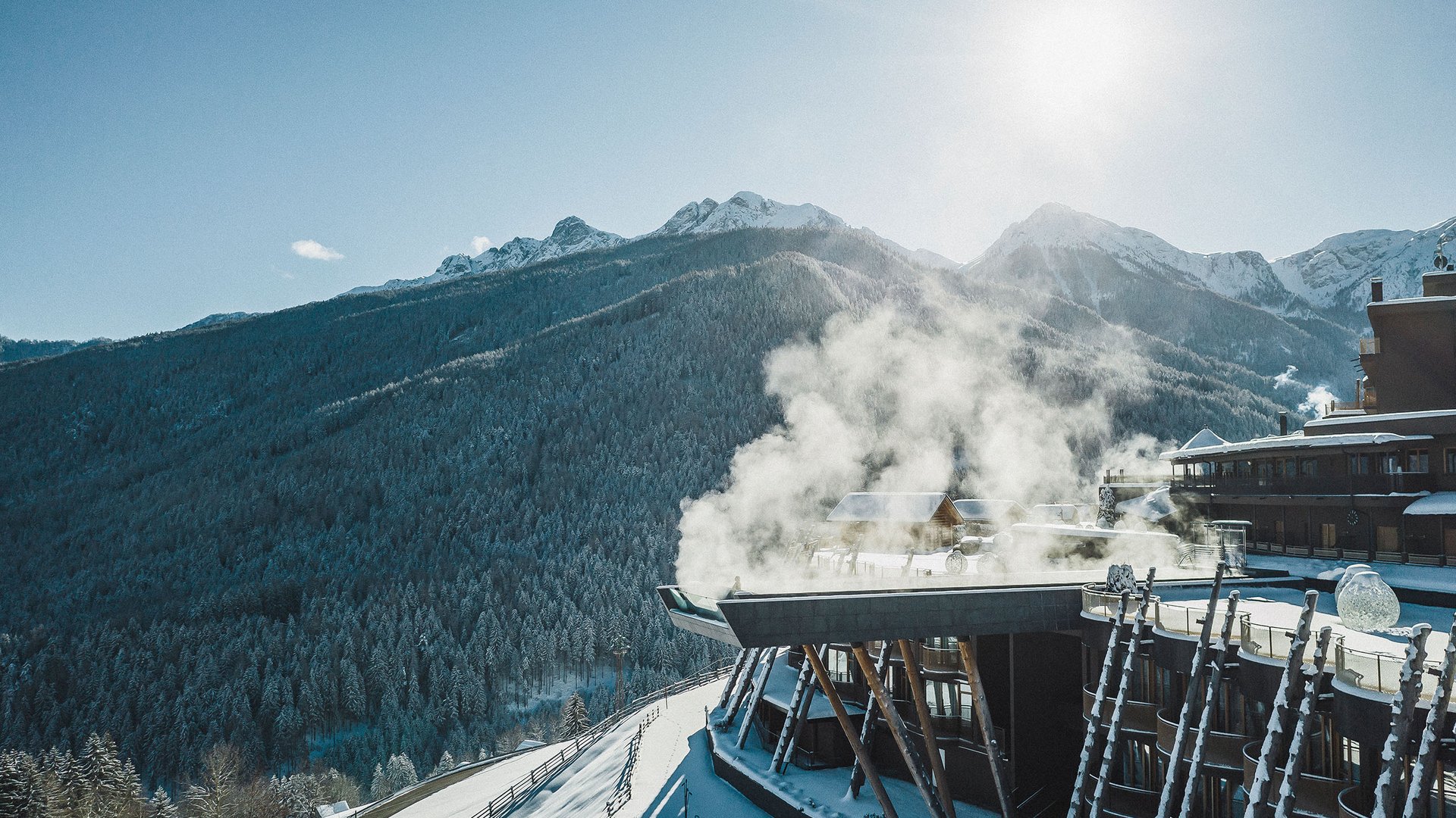 Hotel in Val Pusteria con spa per il vostro relax Hotel di montagna innevato con camino fumante sotto il sole