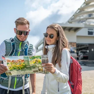 01.10 - 08.11.2026 Couple with backpacks reading hiking map at mountain station