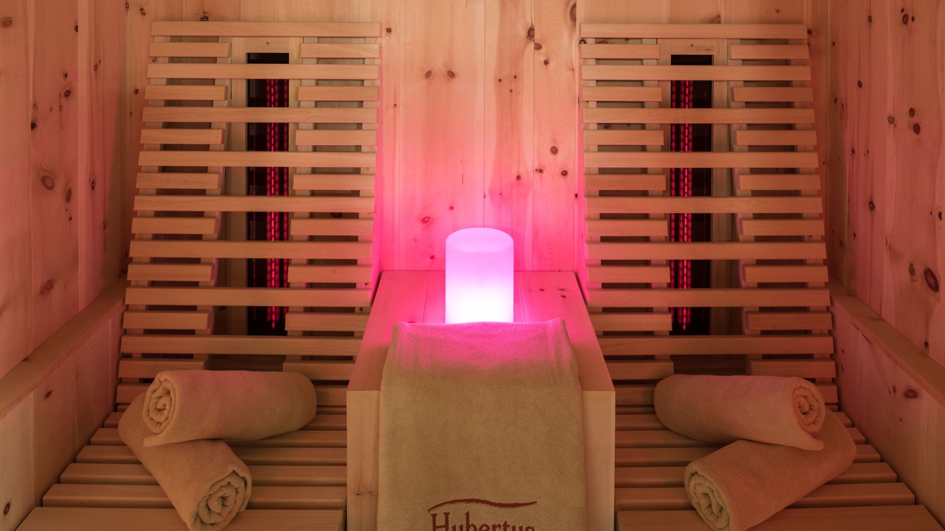 Our sauna, Plan de Corones/Kronplatz in full view Sauna area with wooden loungers, towels, and soft red lighting