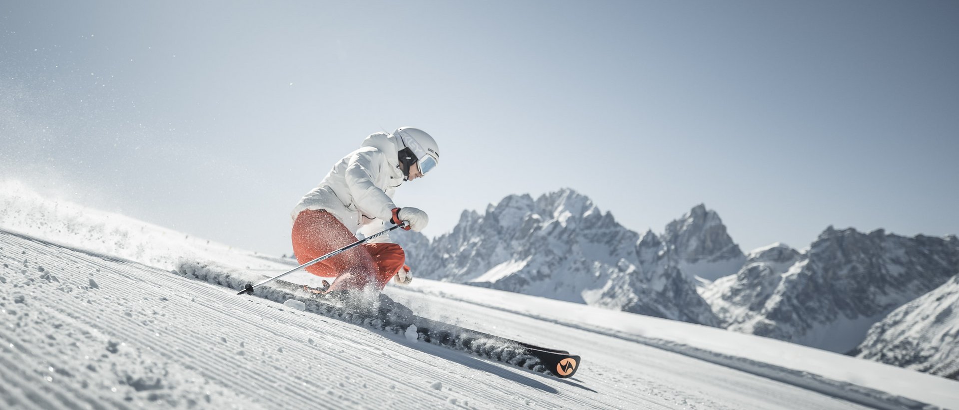 The best hotel at Plan de Corones/Kronplatz Skier in white jacket and orange pants skiing on snowy slope with mountain background