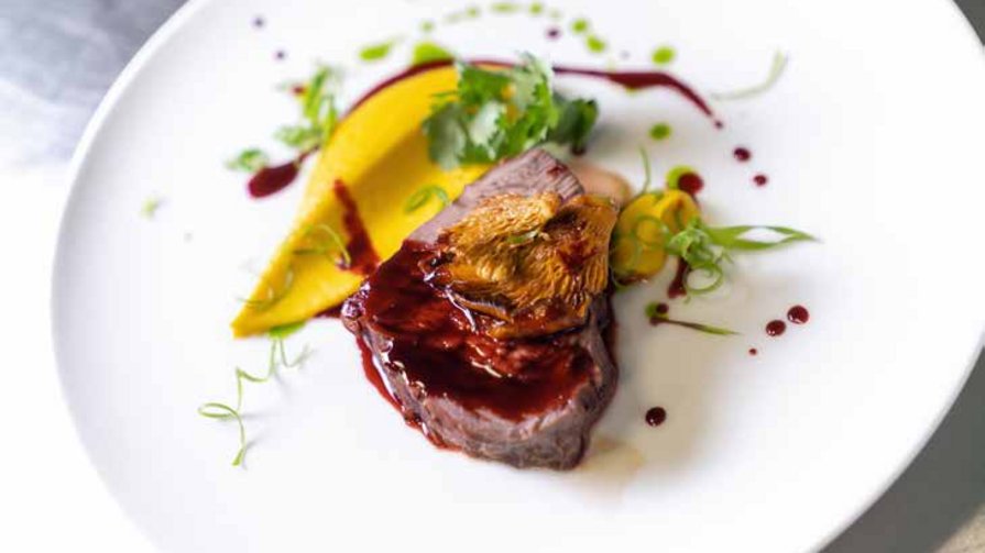 Geschmorte Rindswangen von Chefkoch Antonio Gourmetgericht mit Fleisch, Pilzen und Soße auf weißem Teller angerichtet