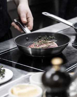 Experience moments of culinary magic Hand holding pan handle with meat and herbs cooking in pan on stove