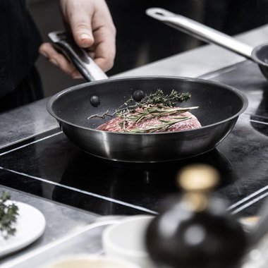 Our family-run hotel in South Tyrol Hand holding pan handle with meat and herbs cooking in pan on stove