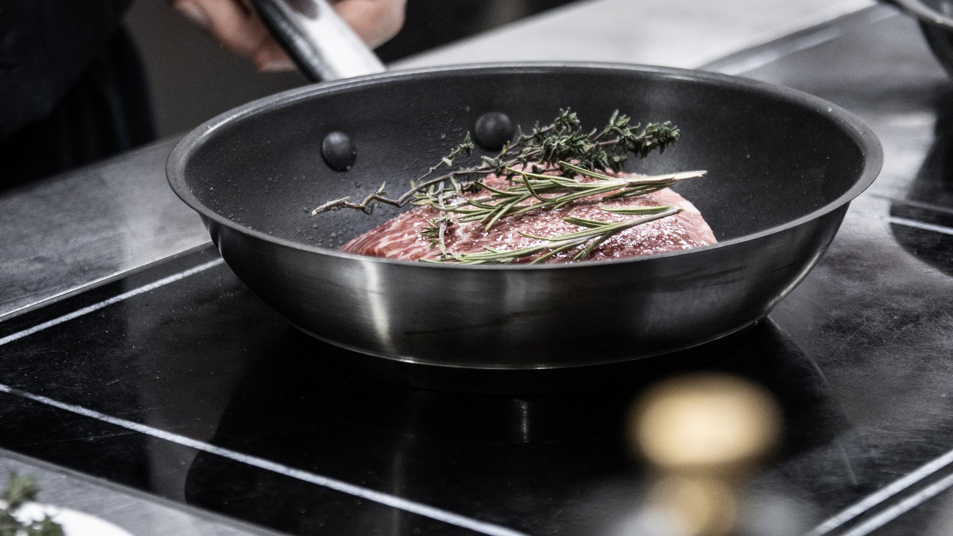 Experience moments of culinary magic Hand holding pan handle with meat and herbs cooking in pan on stove