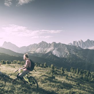 Biken am Kronplatz: einzigartig Zwei Mountainbiker machen Pause auf einer Wiese mit Bergpanorama im Hintergrund