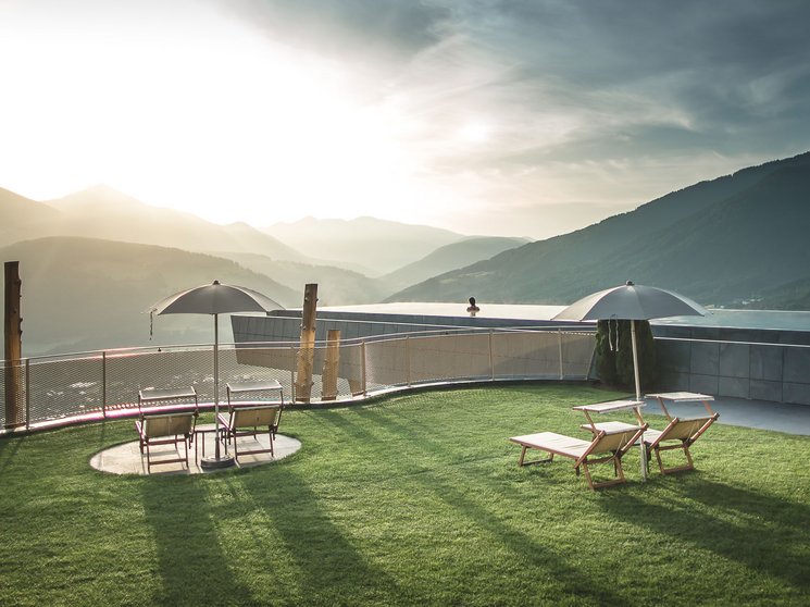 Unsere Parks, Ihre Rückzugsorte Sonnige Terrasse mit Stühlen und Sonnenschirmen vor Berglandschaft bei Sonnenaufgang