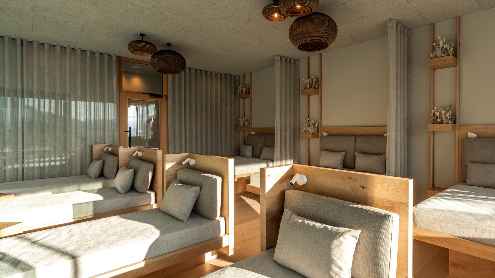 Le nostre saune in Val Pusteria vicino al Plan de Corones Sala benessere luminosa con lettini, rivestimenti in legno e lampade a soffitto in rattan
