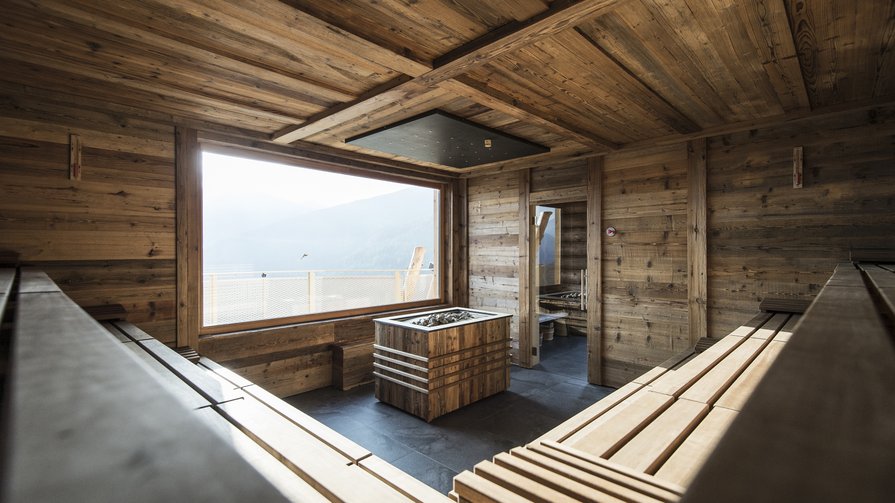 Unsere einzigartige Saunawelt Moderne Sauna mit Holzwänden, Bänken und großer Fensterfront mit Bergblick