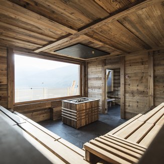 Our wellness hotel in Val Pusteria for relaxation seekers Modern sauna with wooden walls, benches, and large window with mountain view