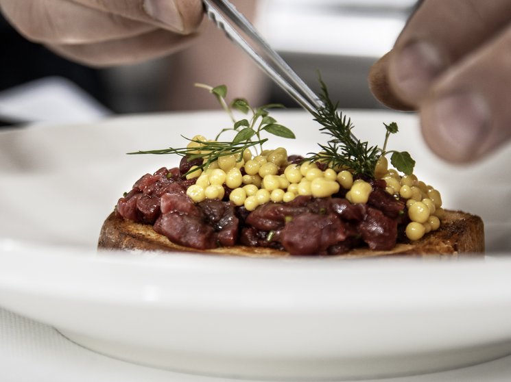 Experience moments of culinary magic Hands decorating a dish with fresh herbs and yellow pearls