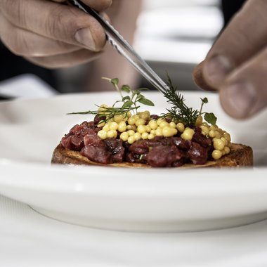 Hotel gourmet in Alto Adige per buongustai Mani che decorano un piatto con erbe fresche e perle gialle