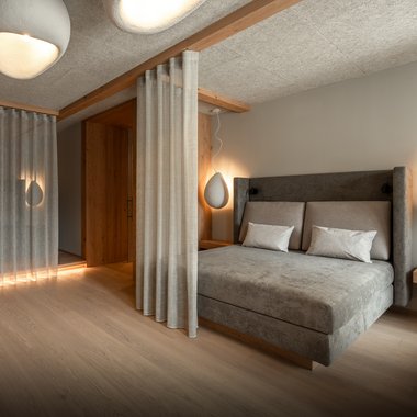 Unser Hotel mit Fitnessstudio in Südtirol Modernes Schlafzimmer mit grauem Bett, Vorhängen und weichen Lampen