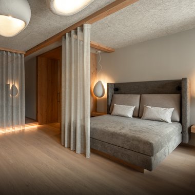 Our hotel with gym in South Tyrol Modern bedroom with gray bed, curtains, and soft lighting
