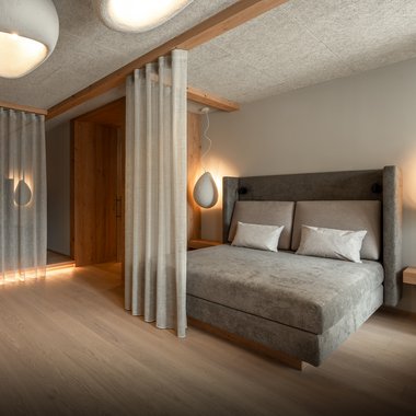 Il nostro hotel con palestra in Val Pusteria Camera da letto moderna con letto grigio, tende e luci soffuse