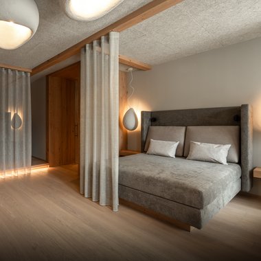 Il nostro hotel con palestra in Val Pusteria Camera da letto moderna con letto grigio, tende e luci soffuse