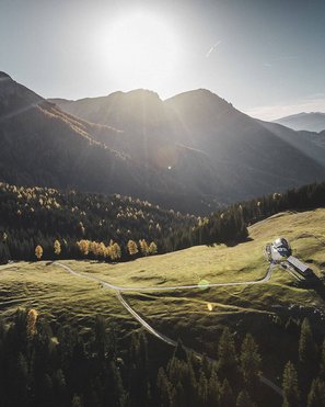 Biken am Kronplatz: einzigartig Sonnenlicht über einer grünen Alm in den Bergen mit einem kleinen Haus