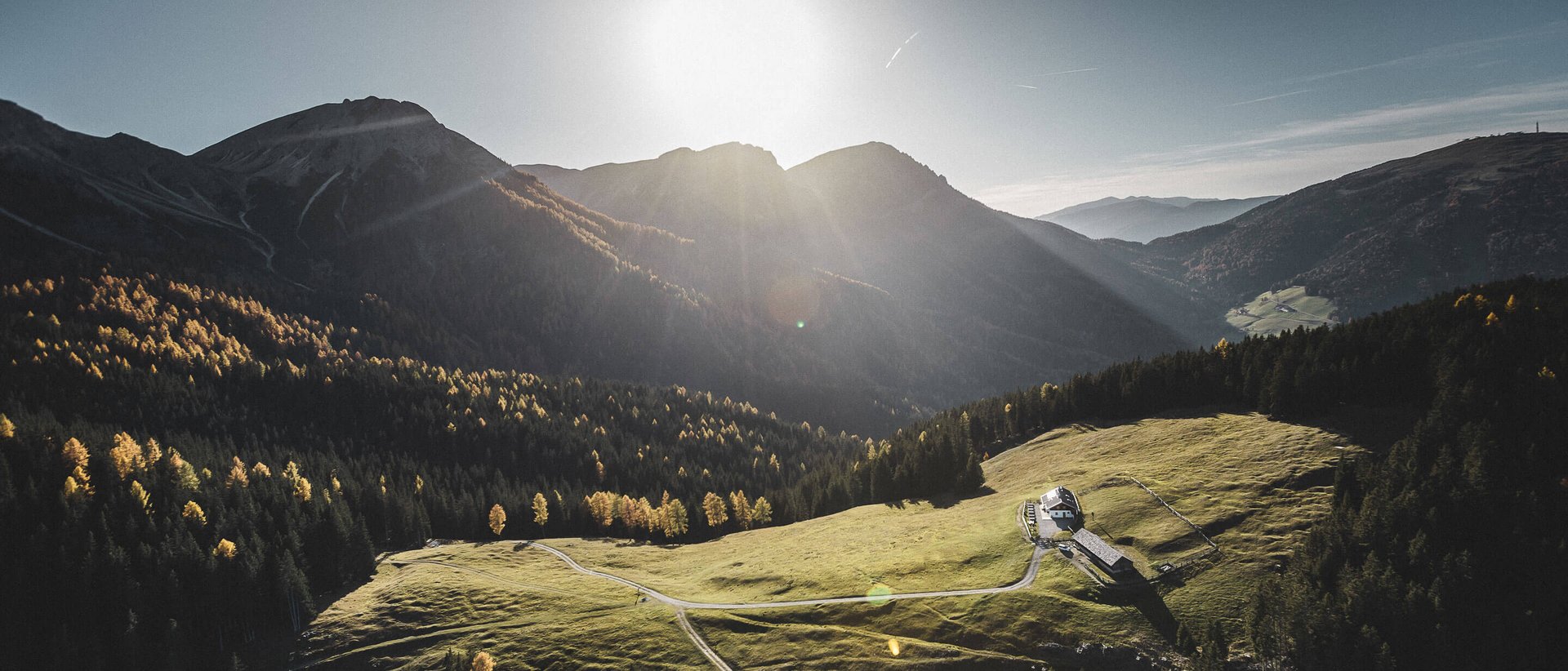 Our wellness hotel in Val Pusteria for relaxation seekers Sunlight over a green alpine meadow with a small house in the mountains