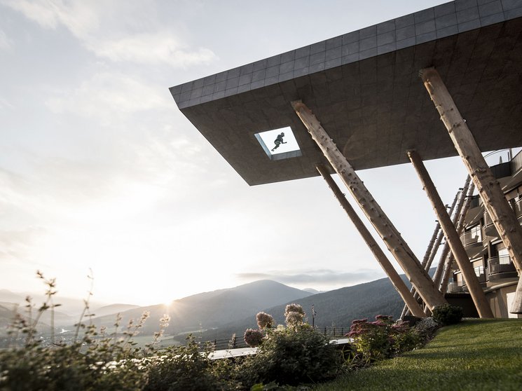 Our wellness hotel in Val Pusteria for relaxation seekers Modern building with wooden supports in front of mountain landscape at sunset