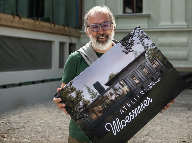 Atelier Moessmer Norbert Niederkofler Uomo tiene un cartello con design architettonico davanti a un edificio storico