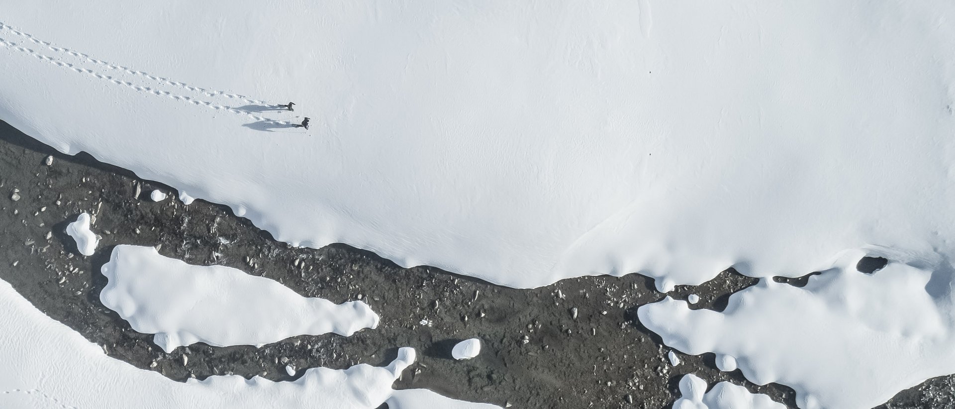 Active holidays in South Tyrol: a great experience Aerial view of two people walking through snow by a river