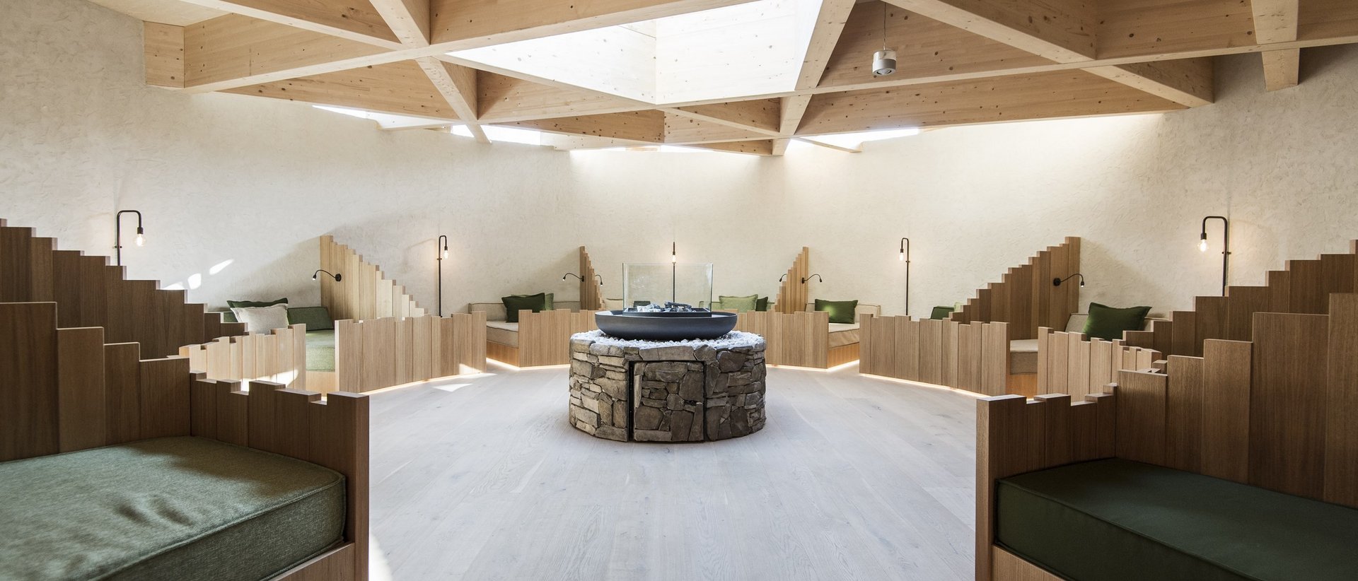 Our wellness hotel in Val Pusteria for relaxation seekers Modern cozy seating area with wooden benches and central stone table under wooden skylight