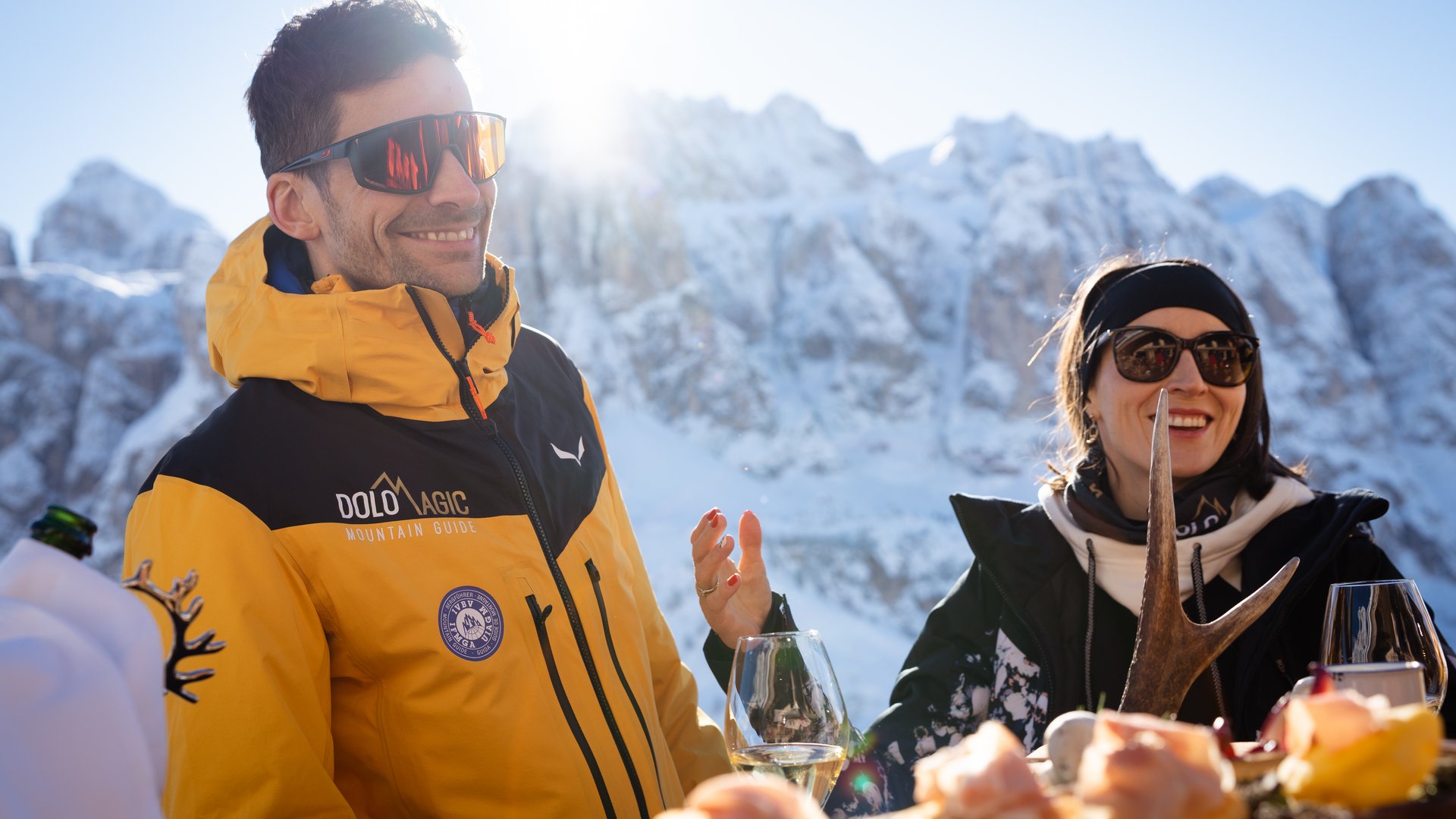 The best hotel at Plan de Corones/Kronplatz Two people dining outdoors in front of snowy mountains on a sunny day
