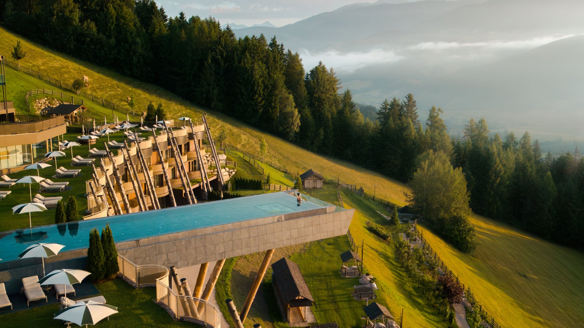 Infinity-Pool auf Holzstützen an Berghang mit Wald und Bergen im Hintergrund