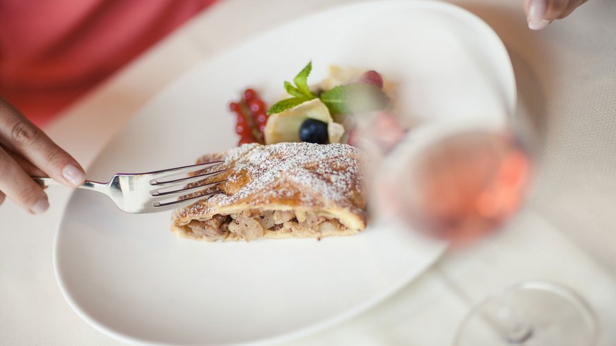 Eine kulinarische Tradition Person schneidet Apfelstrudel mit Beeren auf einem weißen Teller