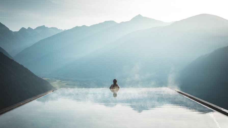 Die Kraft des warmen Wassers Person in dampfendem Infinity-Pool mit Blick auf neblige Berglandschaft