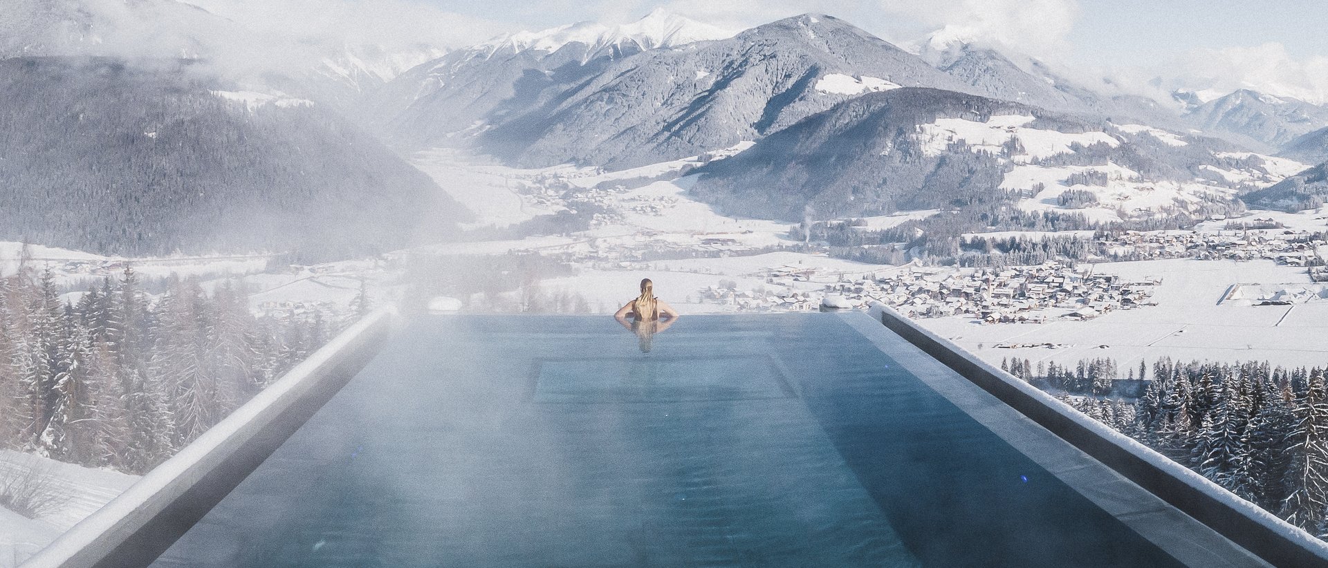 Our current catalogue for downloading Person in heated infinity pool overlooking snowy mountains and valley