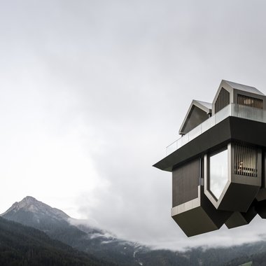 Awards & Press Modernes Architekturgebäude auf Stelzen mit Bergblick und bewölktem Himmel