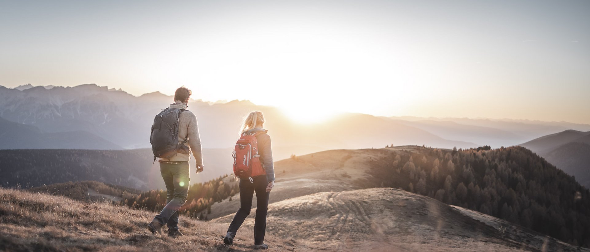 Vacanza a Plan de Corones: un’avventura Due escursionisti con zaini camminano al tramonto in montagna