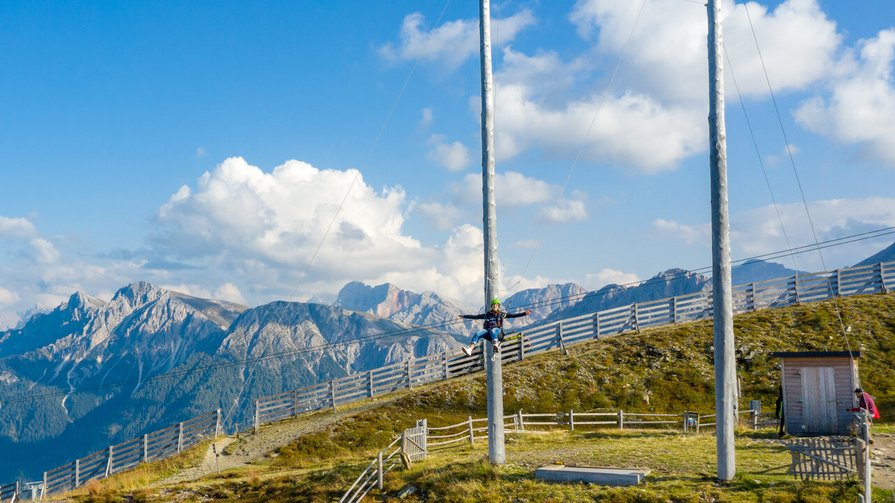 Die Skyscraper-Riesenschaukel auf dem Kronplatz Person klettert an großem Seil auf Berg mit Alpen im Hintergrund