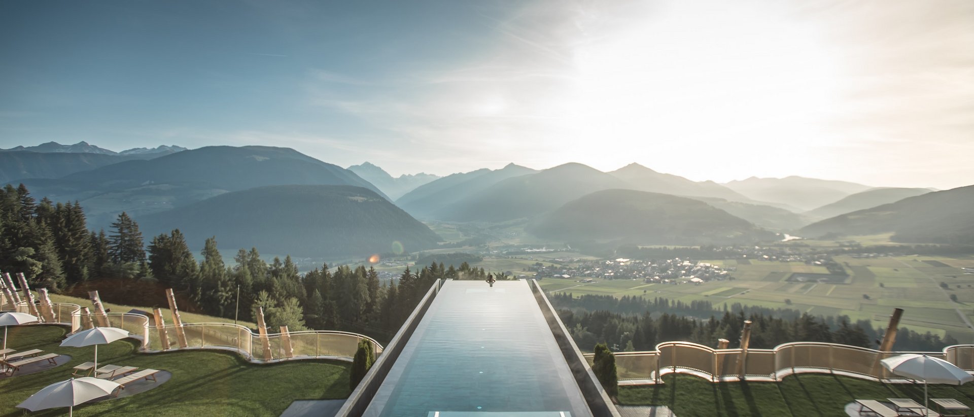 Our wellness hotel in Val Pusteria for relaxation seekers Infinity pool overlooking mountains and valley in sunlight