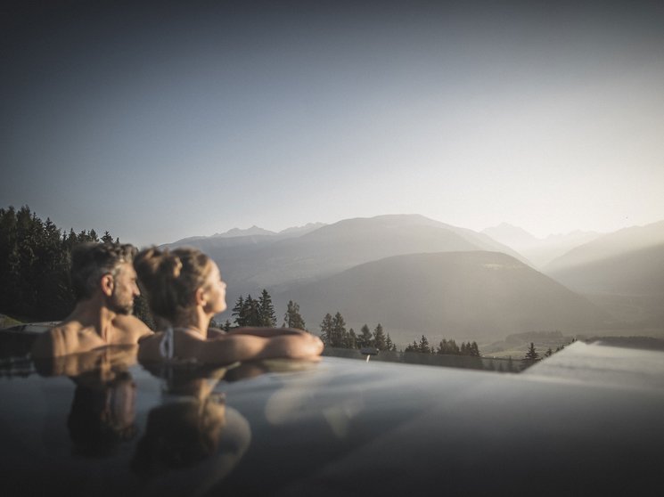 Our wellness hotel in Val Pusteria for relaxation seekers Couple relaxing in outdoor pool overlooking mountains at sunset