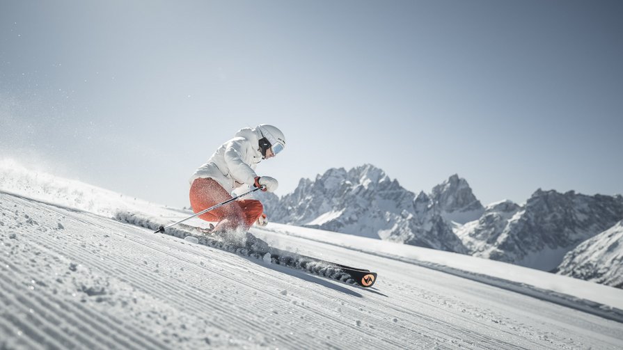 Entdecken Sie das ultimative Skierlebnis im Herzen der Dolomiten Skifahrer fährt auf präparierter Piste vor Bergkulisse bei strahlendem Himmel