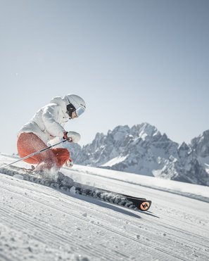 Unser Hotelgutschein: Südtirol im Geschenkformat Skifahrer fährt auf präparierter Piste vor Bergkulisse bei strahlendem Himmel