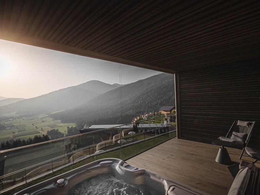 Unser Hotel in Olang zwischen Himmel und Erde Balkon mit Whirlpool und Stühlen mit Blick auf Berge im Sonnenuntergang