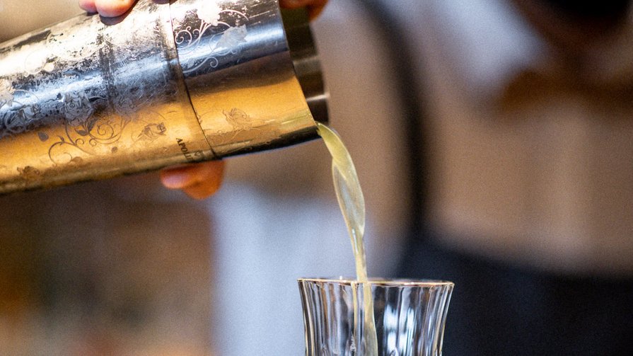 London Dry Gin | fresh lemon juice | basil & cucumber syrup | mango foam Barkeeper pouring green drink from shaker into a crystal glass