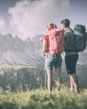 Shopping a Brunico e molto altro ancora Escursionisti con zaini guardano montagne boschive sotto un cielo nuvoloso