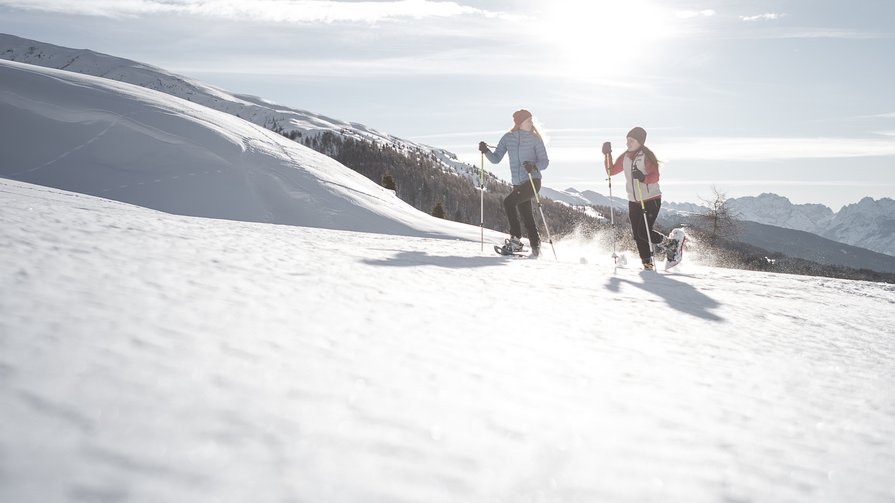 Entdecken Sie die Stille und Schönheit verschneiter Landschaften Zwei Menschen beim Schneeschuhwandern in verschneiter Berglandschaft bei Sonnenlicht