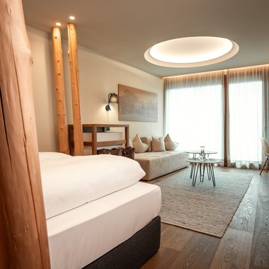 Sustainability Modern hotel room with bed, sofa, tables, and large window with curtains